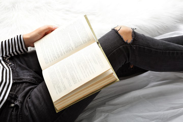 Woman in black jeans reading book on bed top view point
