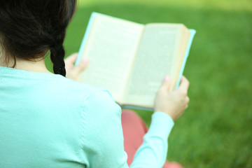 Young woman with book sitting on green grass outdoors