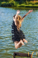 Caucasian Blond Woman in Sexy Dress Jumping Near Water Shore.