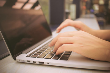 Female hands typing on keyboard of laptop with retro filter effe