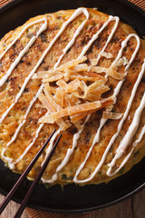 Japanese fast food: okonomiyaki close-up and chopsticks. Vertical

