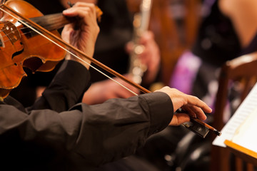 Hands of man playing the violin in the orchestra in dark colors