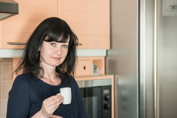 Fototapeta na wymiar Smiling woman drinking coffee at kitchen