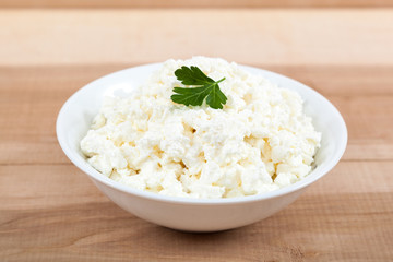 Fresh cottage cheese in a white bowl on a wooden.