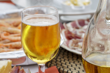 Glass of beer beside a jar of olive oil, shrimps and iberian ham