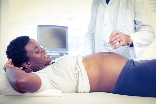 Male doctor performing ultrasound on smiling pregnant woman 
