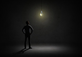 businessman looking at lighting bulb in dark room