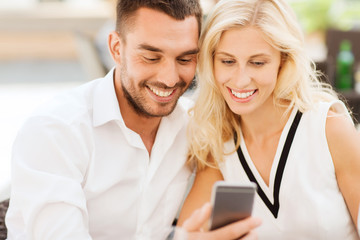 happy couple with smartphone at city street cafe