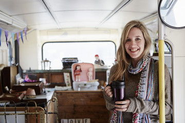 A woman standing in a bus converted into a vintage shop at a flea market surrounded by vintage objects.