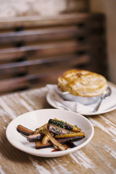 A plate of roasted vegetables cut into batons, and a pie on a tabletop. 