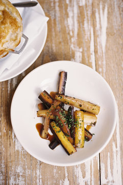 A plate of roasted vegetables cut into batons, and a pie on a tabletop. 