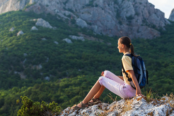 Naklejka na ściany i meble Young woman with backpack sits on rock