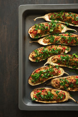 Close up baked eggplants with vegetables on dark pan