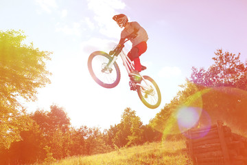 Sportsman on a mountain bike is flying in a jump from a springboard. Photo with special ligth lens effect