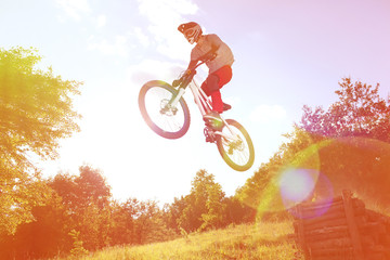 Sportsman on a mountain bike is flying in a jump from a springboard. Photo with special ligth lens...