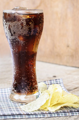 Cold cola soda drink in glass with potato chips