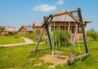 Fototapeta na wymiar Wooden swing on the lawn in the Russian village