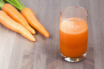 Healthy carrot smoothie in a glass with carrots on wooden background. Shallow dof