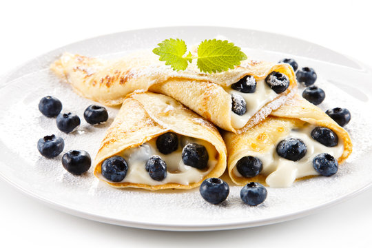 Crepes with blueberries and cream on white background