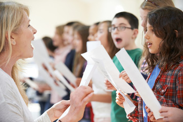Children In Singing Group Being Encouraged By Teacher