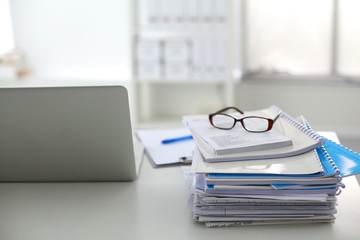 Laptop with stack of folders on table on white background