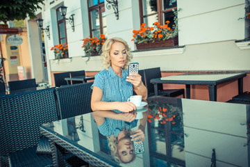 beautiful young girl resting in a cafe. attractive blond model sitting with a cup of coffee in an outdoor cafe of the European city and talking on the phone