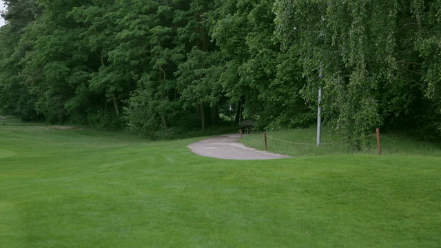 a golf car is driving down a sand path at a golf course. 