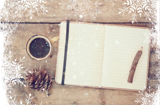 top image of open notebook with blank pages, next to pine cones and cup of coffee over wooden table. top image, glitter overly with snowflakes
