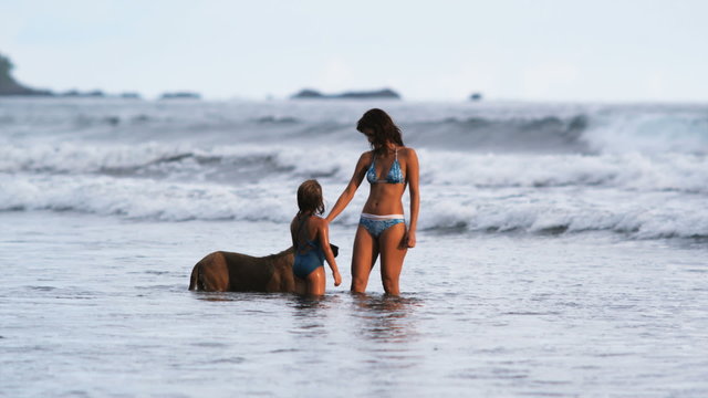 mother and daughter petting a dog in the ocean
