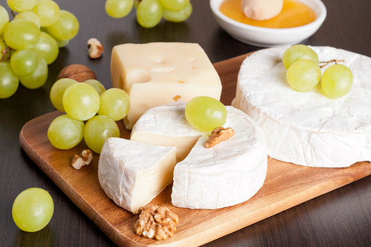 cheeses, honey, grapes and walnuts on a wooden background, horiz