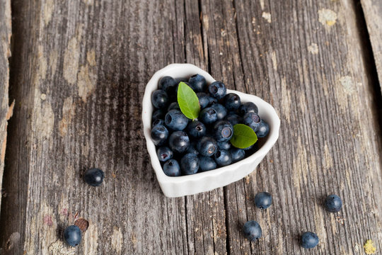Heart shaped bowl of blueberries on wooden table