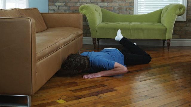 man looking under the couch for his keys