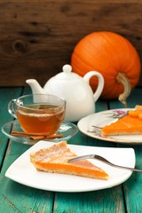 Pumpkin pie, tea in glass cup, white teapot and fresh pumpkin on