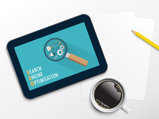 Tablet showing SEO icons on desk with coffee cup, pencil and paper