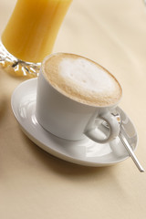 a cup of cappuccino and a glass of orange juice in the background