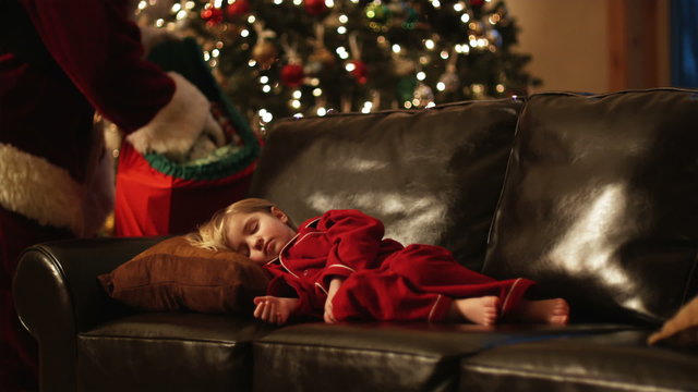 little girl sleeping on the couch while Santa leaves presents