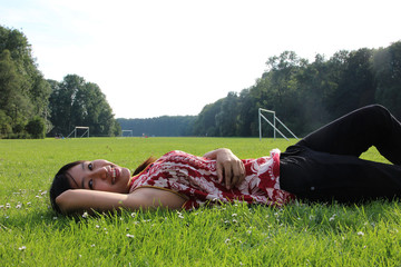A young Asain woman lying on a grass field