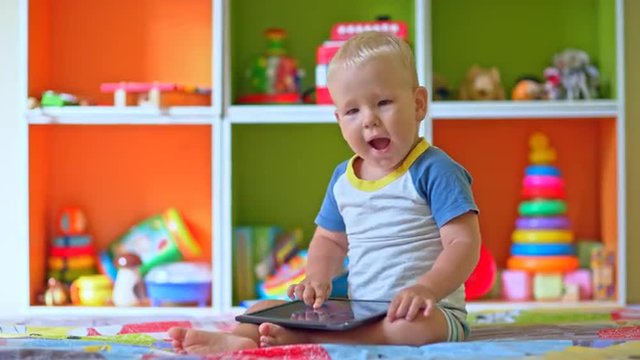 Toddler boy plays with tablet computer in child room