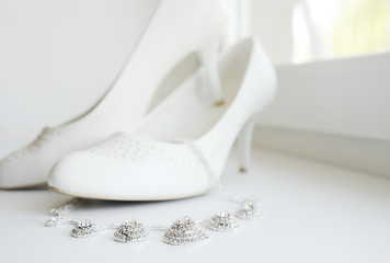 Fototapeta na wymiar White wedding shoes of the bride and the bride's necklace agains