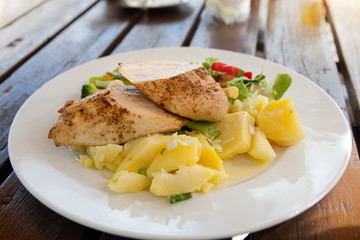 The plate of stewed chicken with boiled potato on wooden table in street cafe
