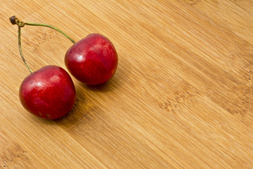 Dojrzałe czerwone owoce czereśni na desce.   Tło z kilkoma owocami czereśni na bambusowej kuchennej desce. © IreneuszB