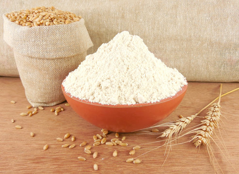 Wheat flour in a bowl and wheat in a sack.
