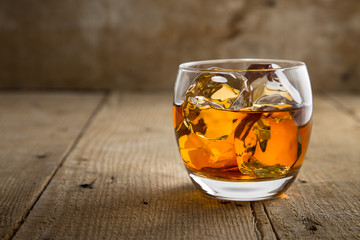 Single glass of whisky bourbon on the rocks golden on old rustic wooden surface open space