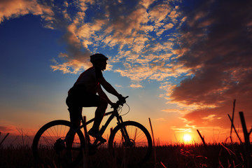 Obraz premium Silhouette of a biker and bicycle on sunset background.