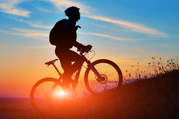 Obraz premium Silhouette of a biker and bicycle on sunset background.