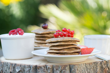 Breakfast in the garden: paleo style grain free banana almond pancakes, coconut yogurt with berries, selective focus on redcurrants