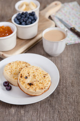 Hot toasted crumpets on the wooden table with blueberries and jam on the back, selective focus