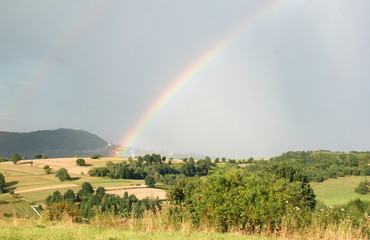 Podwójna kolorowa tęcza na tle zielonych pól w słoneczny letni dzień © siwyk