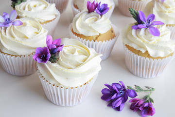Homemade purple freesia flowers on vanilla cupcakes with whipped
