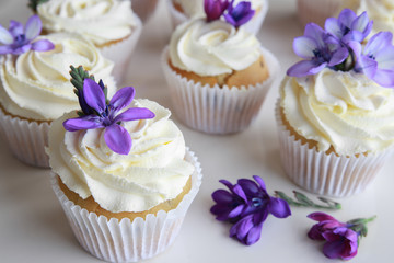 Homemade purple freesia flowers on vanilla cupcakes with whipped cream frosting